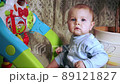 pensive baby sits near developing toy and looks at camera 89121827