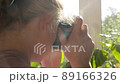 Young woman with blond curly hair photographs nature through the window 89166326