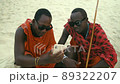 Happy Maasai Tribe Men Sitting on the Sand in the Desert Watching Smartphone and Showing Thumb Up Sign. 89322207
