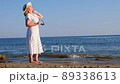 woman in a straw hat and white dress puts on sunglasses and walks along the seashore and admires the 89338613