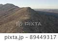 Aerial shot from a drone gliding up and over a tall, steep, long mountain ridge, with a view of a wide valley and mountains  beyond 89449317