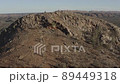 Aerial shot from a drone rising up and over a mountain, with a view of a wide valley and mountains beyond 89449318