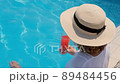 fashionable blonde woman in straw hat relaxes and drinks orange cocktail near the swimming pool on a 89484456