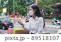 Young asian woman sitting on the bench and using smartphone with paper shopping bags after shopping in the park near street. 89518107