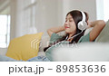 Young asian woman listening to music on couch in living room at home 89853636