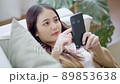 Happy young asian woman relax on comfortable couch at home texting messaging on smartphone 89853638