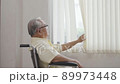 Old asian man sits in a wheelchair and looks out the window 89973448