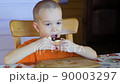 Boy sitting on a chair in a kitchen and eating the sandwich with strawberry 90003297