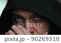 A man with a beard in the hood looks sadly at the camera and rubs his eyes with his hands, static camera, close-up of the face 90269310