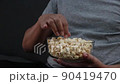 Man eating popcorn in a glass cup on the sofa while watching movies at home. 90419470