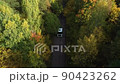 One Semi Truck without trailer traveling alone on dense flat forest asphalt straight empty road. Amazing aerial perspective of truck among the woods. Tall pine trees in forest. Autumn trees. 90423262