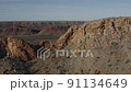 Drone wide view of a gap in the rocks on a steep, mountain ridge, with a view of other ridges in the background 91134649