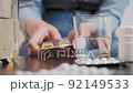 A young woman takes out a tablet from a bottle, takes a glass of water and takes the medicine. There are many tablets on the table, blurred background 92149533