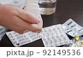 A young woman opens a bottle and pour pills from a bottle into her hand, then holds it, close-up 92149536