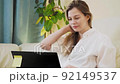 A young woman sitting on a couch and working on her laptop at home, chatting, look at her phone, typing 92149537