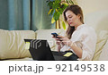 A young woman sitting on a couch and working on her laptop at home, chatting, look at her phone, typing 92149538