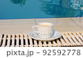 White cup of coffee or hot drink on the background of a blue swimming pool on a summer sunny day 92592778