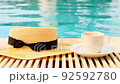 Close-up of a cup of coffee and a straw hat on the background of a blue swimming pool on a summer 92592780