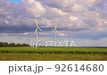 Panoramic landscape view of new white modern wind turbine farm power generation station against clear blue sky canola field. Clean sustainable zero emission alternative electricity windfarm industry 92614680