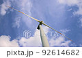 Bottom up view of new white modern wind turbine farm power generation station against clear blue sky cloudscape. Clean sustainable zero emission alternative electricity windfarm industry 92614682