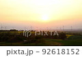 Panoramic landscape view of many modern wind turbine farm power generation station against warm sunset haze mist sky. Clean sustainable zero emission alternative electricity windfarm industry 92618152