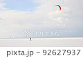 Minimalism scenic view of adult man enjoy extreme sport activities riding kite surfing board on white desert snow frozen lake surface against blue sky. Winter outdoors adventure lifestyle 92627937
