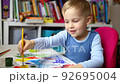 Portrait of cute little blond kid boy enjoy have fun painting with watercolor and brush bright abstract inage on paper at home or kindergarten class. Imagination development children play activity 92695004