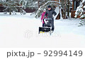 Father teaches his daughter in backyard of suburban house to remove snow with snowplow. Positive emotions, family outdoor recreation. Real people. Child helps with housework. Slow motion, 4k. 92994149
