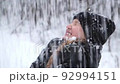 Snow falls on the face of a laughing teenage girl in winter clothes, in a park or forest. Portrait of a girl 10-11 years old with enjoying snowfall. Loud laugh with open mouth. Slow motion 92994151
