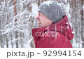 Snow falls on the face of a laughing man in winter clothes, in a park or forest. Portrait of a young man with a friendly face enjoying snowfall. Real people, lifestyle, Christmas holidays. Slow motion 92994154