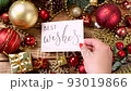 Woman's hand putting a Christmas card with the text BEST WISHES on a wooden table 93019866