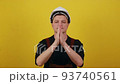 A young caucasian guy wearing a hard hat and builder clothes over isolated yellow background prays with his hands with a hopeful expression on his face and then rejoices in success 93740561