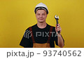 Friendly plumber foreman or handyman in hardhat holding adjustable wrench and hammer on yellow isolated background 93740562