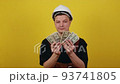 Foremans salary. Close-up photo of a happy young man in a suit and construction helmet, who is holding a wad of cash in his right hand and showing thumbs up. 93741805