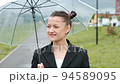 A woman in a black jacket under a transparent umbrella, on the street of the city, outdoors. Rain. 94589095