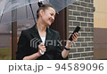 A woman in a black jacket under a transparent umbrella, on the street of the city, outdoors. Rain. 94589096