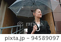 A woman in a black jacket under a transparent umbrella, on the street of the city, outdoors. Rain. 94589097