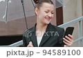 A woman in a black jacket under a transparent umbrella, on the street of the city, outdoors. Rain. 94589100