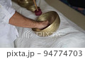 A hand moving a wooden stick along a border of a tibetan singing bowl during healing sound therapy A hand moving a wooden stick along a border of a tibetan singing bowl during healing sound therapy 94774703