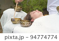 Young woman laying on a massage bed during a sound massage therapy with tibetan singing bowl outdoor Young woman laying on a massage bed during a sound massage therapy with tibetan singing bowl outdoor 94774774