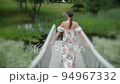 tall woman in a floral dress walks on a white bridge by the lake in summer 94967332