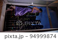 rich woman in a purple dress standing by the window and looks at the night city with skyscrapers. vertical 94999874
