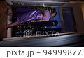 rich woman in a purple dress standing by the window with a glass of champagne and looks at the night city with skyscrapers. vertical 94999877