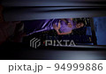 rich woman in a purple dress standing by the window with a glass of champagne and looks at the night city with skyscrapers. vertical 94999886