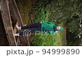 a woman in a green sweater, hat and sunglasses stands on an old wooden boat by the lake in autumn in the village. Vertical 94999890