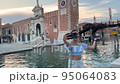 funny energetic woman makes video call using mobile internet on her smartphone. she is a tourist walking around Venice in Italy and posing against the backdrop of the Arsenal 95064083