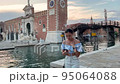 Young woman tourist got lost in venice and looks at the map on her mobile phone. A brunette woman admires the scenery of Venice at sunset. the woman is a little puzzled 95064088