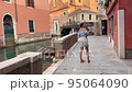 Young woman tourist got lost in venice and looks at the map on her mobile phone. A brunette woman admires the scenery of Venice at sunset. the woman is a little puzzled 95064090