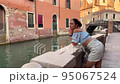 one person, a woman 30 years old in a blue top. leaning on a brick wall, she looks at the Venetian canal. She is romantically dressed in a blue top and denim shorts. 95067524