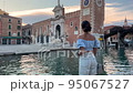 one person, a woman 30 years old. woman tourist visiting the Arsenal landmark in venice italy. She is romantically dressed in a blue top and denim shorts. 95067527